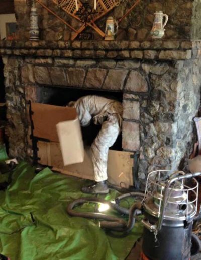 man in white suit climbing into fireplace in home with green drop cloth on floor and vaccum cleaner