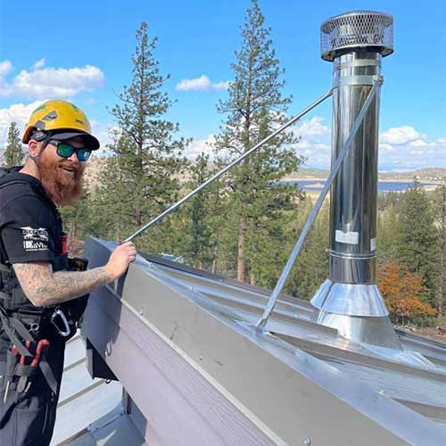 Chimney Tech wearing yellow helmet with long red beard holding a rope wrapped around new metal chimney