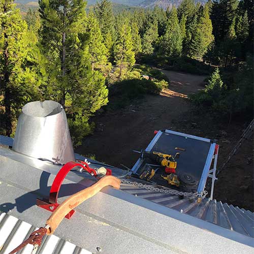  View from the top of a roof where a metal chimney is being installed to the left rope and tools are seen as well