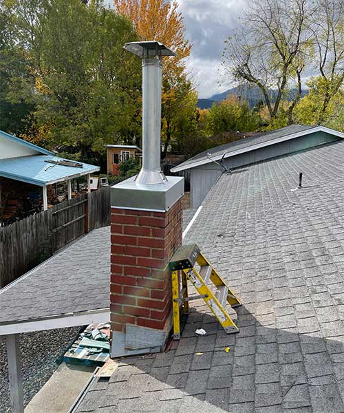 Newly built chimney on roof with short yellow step ladder leaning against it grey shingles on roof