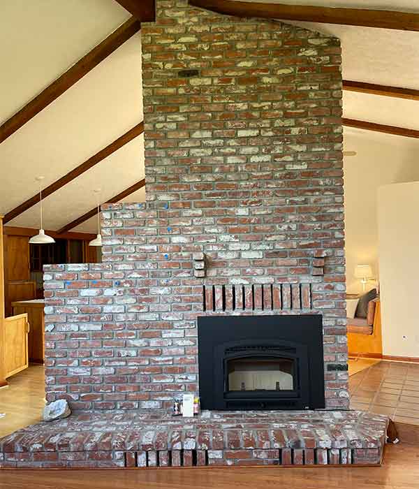 large brown and white bricked fireplace in home with a black chimney insert in it