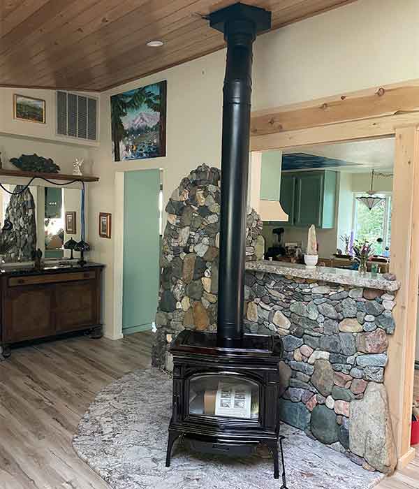 Free standing wood stove in front of rock bricked wall in home doorway seen in the background