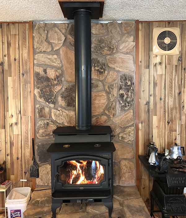 Black Free standing wood stove in room of home rock background on wall and wood to the sides a small table with items on it to the right