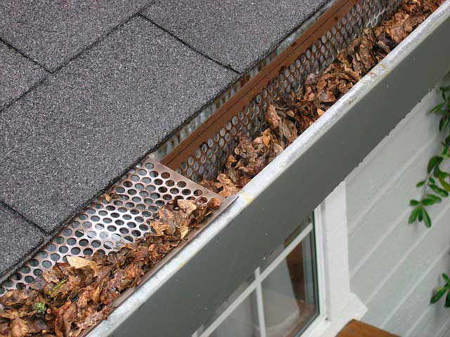 Roof of home with close up of gutters they are filled up with leaves