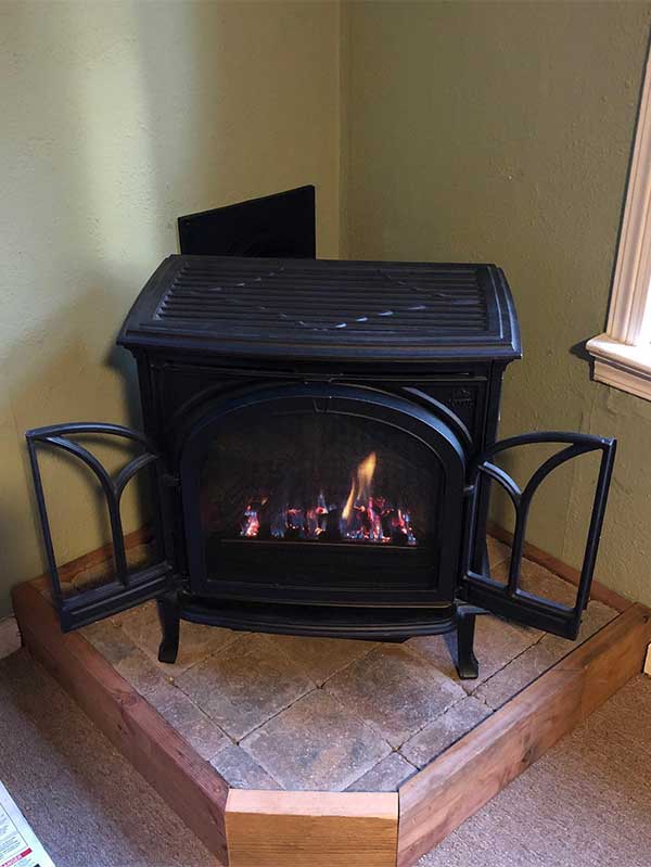 Small Black Wood stove in corner of a room with its doors open sitting on a wooden platform