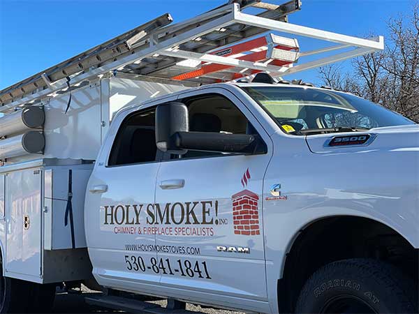 White pickup truck with ladders in top of it with Holy Smoke Chimney and Fireplace Specialists on door