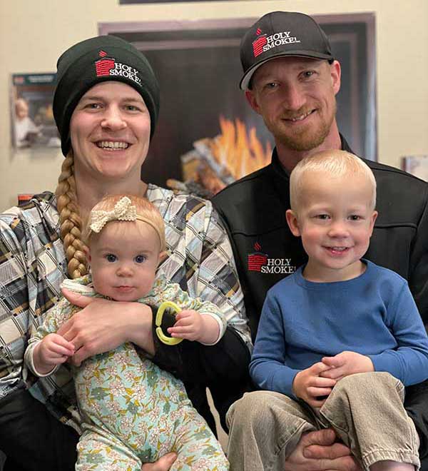 Man and woman wearing black sock hats and each holding a small child all are smiling