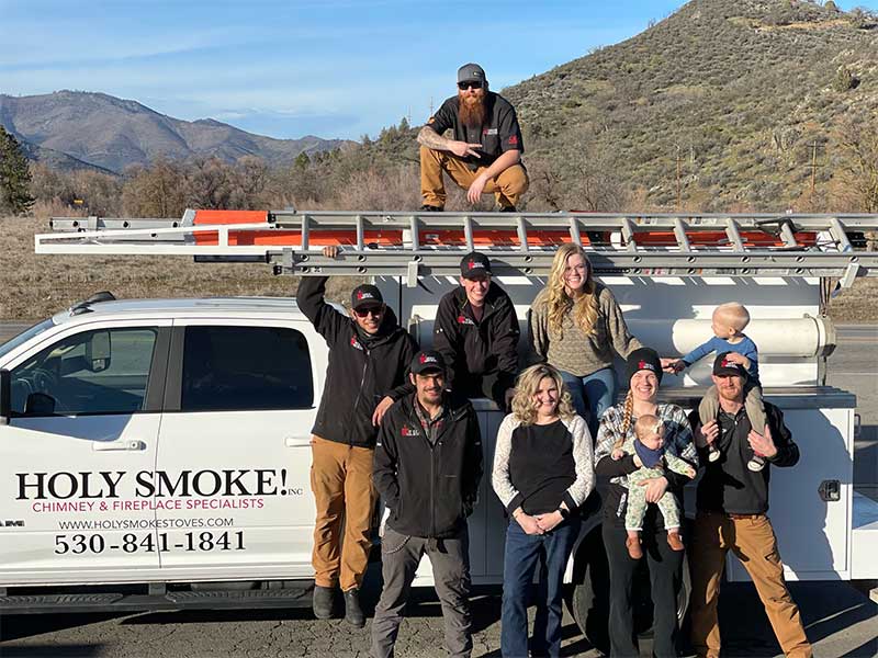 Group of men and women standing in front of Holy Smoke Work truck with ladders on top