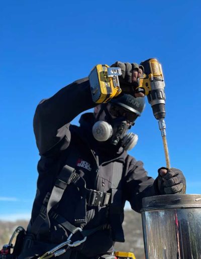 Man in black helmet and clothing with respirator using a drill and tool on the chimney on roof