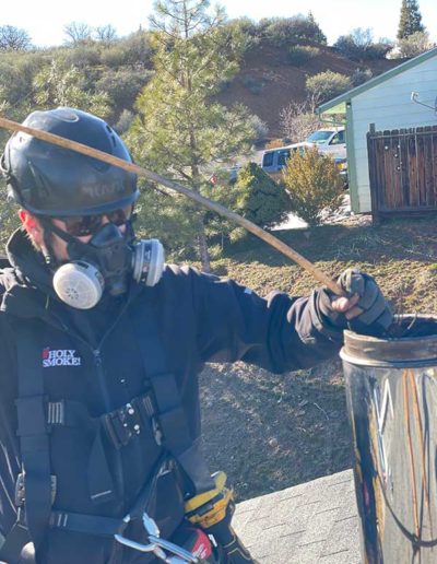 man with black helmet and coat wearing a respirator lowering cleaning tool into a chimney