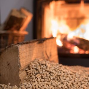 a wood log next to some wood pellets with a burning fireplace in the background
