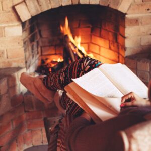 a person wearing comfortable pants, reading a book by a fireplace