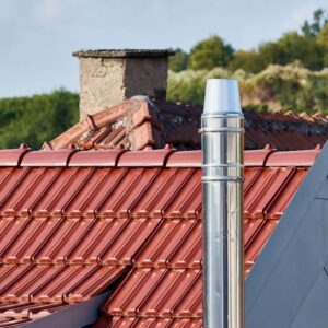 a shiny metal chimney flue with a stone chimney in the background